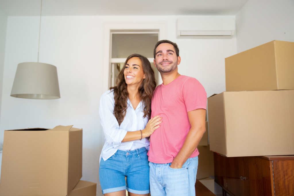 Comprar ou alugar em 2025? Descubra o que faz mais sentido para sua vida financeira. 2 casal alegre olhando seu novo apartamento caminhando entre caixas de papelao e se abracando